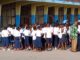 En avant plan de droite à gauche en chemise verte un enseignt en conversation avec des élèves habillés en bleu blanc devant le batiment d'une école à Kinshasa Radio Okapi Ph John Bompengo