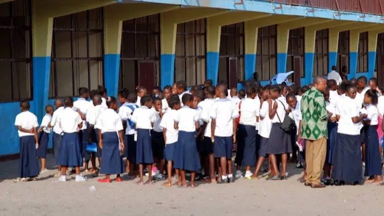 En avant plan de droite à gauche en chemise verte un enseignt en conversation avec des élèves habillés en bleu blanc devant le batiment d'une école à Kinshasa Radio Okapi Ph John Bompengo